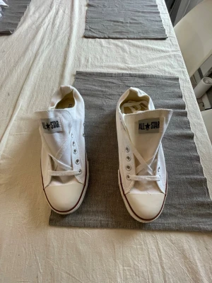 Vita Converse All Star låga sneakers - Klassiska vita Converse All Star sneakers i canvas med lågt skaft och vit gummisula. Skorna har den ikoniska All Star-loggan på plösen och metallöljetter för snörning. Perfekta för en avslappnad och stilren look.