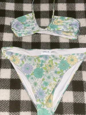 Blommig bikini från Gina Tricot - Säljer en superfin bikini från Gina Tricot. Bikinin har ett blommigt mönster i pastelliga färger som ljusgrön, gul och lila. Överdelen har smala axelband och underdelen är klassiskt skuren. Perfekt för sommaren!