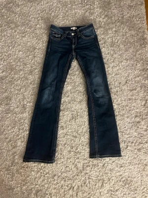 Mörkblå bootcut jeans/dżinsy - Snygga mörkblå bootcut jeans med vita kontrastsömmar och klassiska fem fickor. Jeansen har låg midja och en lätt tvättad look. Perfekta för dig som gillar en tidlös och cool stil.