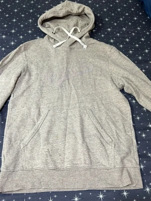 Grå hoodie från Roaddale - Grå hoodie från Roaddale med tryckt logga på bröstet. Klassisk känguruficka framtill och justerbar huva med vita snören. Tillverkad i mjukt sweatshirtmaterial, perfekt för kalla dagar.