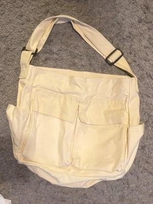 Beige tygväska - Ljus beige/crame vit tyg axel väska med fickor på framsidan och en ficka innuti💛 den är helt oanvänd