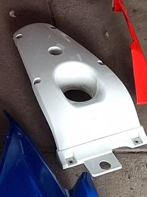 Vit plastkåpa till moped - Vit plastkåpa med flera monteringshål och en större öppning i mitten, troligen avsedd för moped eller motorcykel. Kåpan har en avlång form och är tillverkad i hård plast. Perfekt för dig som behöver reservdelar eller vill byta ut en trasig kåpa.