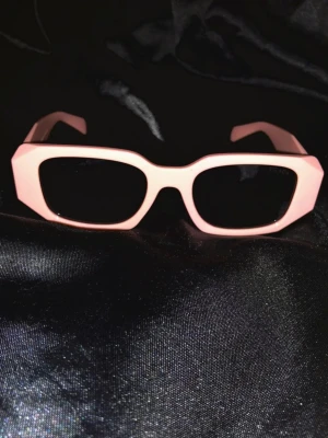 Prada Rosa Glasögon  - Rosa Prada-glasögon 💖 för en oemotståndlig look! Fånga blickar och utstråla elegans med dessa trendiga solglasögon. Perfekta för soliga dagar och stilfulla äventyr ☀️😎. Missa inte chansen att äga ett par ikoner! ✨