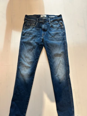 Replay Anbass jeans mörkblå - Snygga blå slim fit jeans från Replay med lätt slitna detaljer och klassisk femficksdesign. Jeansen har en medelhög midja och är tillverkade i stretchigt denim för extra komfort. Perfekta för en trendig och avslappnad look. Replay Anbass W31 L32. Bra skick förutom en liten slitning i skrevet(se bild).