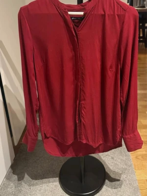 Mörkröd blus med långa ärmar - Stilren mörkröd blus med långa ärmar och klassisk krage. Blusen har en rak passform och dolda knappar framtill. Perfekt att matcha med jeans eller kjol för en snygg look. 