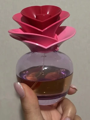 Parfym EDP 100ml flaska  - Justin Bieber ”Someday” 100ml från början ca 50ml kvar. Unik parfymflaska med ett iögonfallande lock format som en blomma i flera lager av rosa och rött. Flaskan är rund och genomskinlig med lila ton och innehåller bärnstensfärgad parfym. Perfekt som dekoration på sminkbordet eller i badrummet.