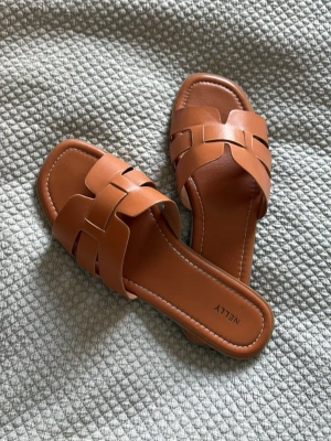 Bruna slip-in sandaler från Nelly - Snygga bruna slip-in sandaler från Nelly med flätad design över foten och fyrkantig tå. Jättefina men har bara inte kommit till användning💕