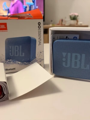 JBL Go Essential bärbar högtalare blå - JBL Go Essential är en kompakt och smidig bärbar högtalare i blå färg. Den har en rektangulär form, tydlig JBL-logga på framsidan och är tillverkad i plast med metallgaller. Ansluts via Bluetooth och är vattentålig, perfekt för musik på språng.