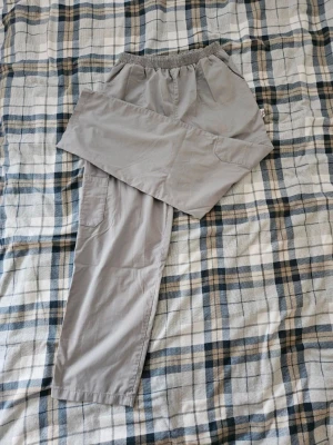 Grå cargo pants - Bekväma grå cargobyxor i storlek M. Resår i midjan. Byxfickor i sidorna och större benfickor med dragkedja på låren. 100% bommul.