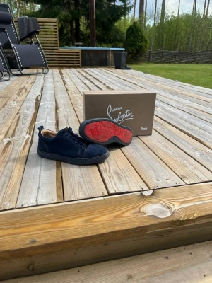 Mörkblå Christian Louboutin sneakers - Snygga mörkblå sneakers från Christian Louboutin i mocka med klassisk röd sula. Lågt skaft och svarta skosnören. Kommer med originalkartong och dustbag. Perfekta för dig som vill sticka ut med exklusiva detaljer och stilren design. Billigare vid snabb affär.