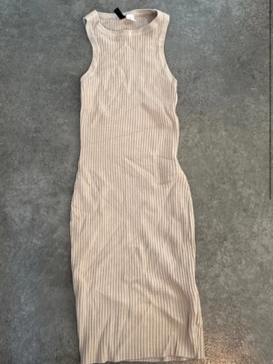 Beige ribbad ärmlös klänning - Snygg beige ribbad klänning i kroppsnära modell. Klänningen är ärmlös med rund halsringning och har en mjuk, stretchig känsla. Perfekt för dig som gillar en enkel men trendig look. Är storlek xs men är mycket töjbar så passar till iallafall M