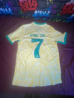 Brasilien Vini Jr. matchtröja gul - Säljer en gul Brasilien fotbollströja från Nike med gröna detaljer, nummer 7 och VINI JR. på ryggen. Tröjan har officiellt Brasilien-emblem på bröstet och är tillverkad i ett lätt, ventilerande material. Perfekt för dig som älskar fotboll och vill stötta landslaget.