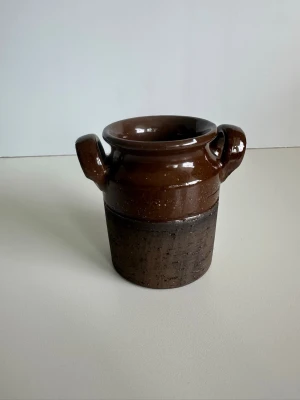 Brun keramisk vas / urna / kruka med två handtag - Stilren brun urna / vas / kruka i keramik med två handtag. Urnan har en glansig yta upptill och en matt, texturerad yta nedtill. 10cm hög och 9cm i diameter. Perfekt som dekoration, vas för blommor eller för plantering av växter. Fint skick!