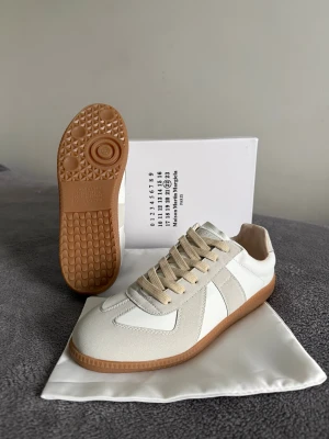 Maison Margiela skor - Maison Margiela  skor i vitt och beige med klassisk gummisula. Skorna har ovandel i skinn och mocka, beige snörning och diskret design. Perfekta för dig som gillar minimalistisk och stilren look.