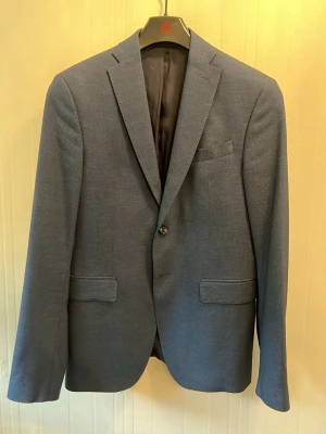 Mörkblå kavaj från ZARA - Snygg mörkblå kavaj från ZARA med klassisk passform och två fickor framtill. Kavajen har ett smalt slag, en knappstängning och innerfoder med randigt mönster. Perfekt för en stilren look och enkel att matcha med skjorta eller t-shirt.