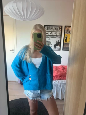Blå oversized kofta med fickor - Mysig oversized blå stickad kofta med två stora fickor framtill och djup V-ringning i mohair. Koftan har ribbade muddar och stängs med tre knappar. Superfint skick bortsett från små noppror på tyget.