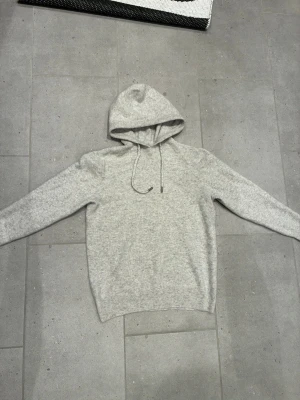 Kashmir tröja  - Snygg ljusgrå hoodie med huva och dragsko. Mjuk och skön känsla, perfekt för en avslappnad stil. Klassisk passform med långa ärmar och ribbade muddar. Passar till jeans eller mjukisbyxor för en chill look.