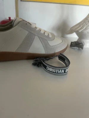 Christian Dior svart tygarmband - Svart och vitt tygarmband från Christian Dior med texten 'Christian Dior J'Adior'. Armbandet har tofsar i ändarna och är justerbart för att passa olika handleder. Perfekt accessoar för att ge din stil en exklusiv touch.