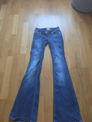Blå bootcut jeans från 157 - Snygga blå bootcut jeans från 157 med klassisk femficksdesign och låg midja. Jeansen har utsvängda ben och är tillverkade i denim med lätt tvättad look. Perfekta för en avslappnad och trendig stil. Har lite defekter vid ben kanten.