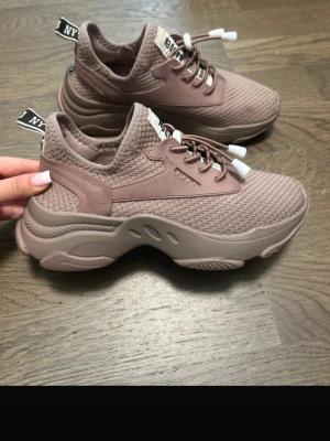 Chunky rosa sneakers med mesh - Snygga chunky sneakers i dammigt rosa med grov sula och stickad mesh upptill. Skorna har elastiska snören med vita detaljer och dragflik baktill med NY-logga. Perfekta för en trendig streetstyle-look.