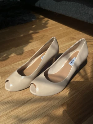 Nude open toe pump klackar från Clarks - Nude/beige oanvända klackskor i patent äkta läder från Clarks!💛 Originalpris på 895kr. 💛 Skickas med box, skorna endast provade inomhus av mamma och är helt i nyskick, boxen är i OK skick då den stått i en garderob ett tag. Står hemma hos min mamma, så hon skickar dem samma dag man köper! Finns fler bilder på skorna. Pris går att diskutera 💛