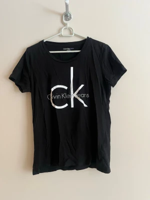 Svart Calvin Klein t-shirt med logga - Snygg svart t-shirt från Calvin Klein Jeans med stor vit CK-logga framtill. Klassisk rund halsringning och korta ärmar. Tillverkad i mjuk bomull som känns skön mot huden. Perfekt till jeans eller shorts för en clean och enkel look.