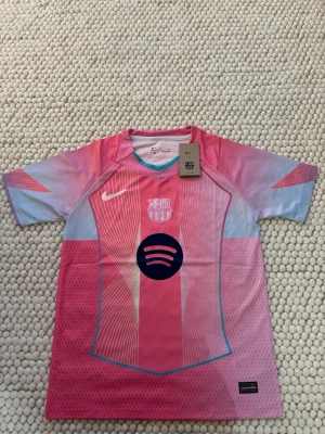 Nike FC Barcelona rosa matchtröja - Säljer en FC Barcelona matchtröja från Nike i rosa och ljusblått med vita detaljer. Tröjan har klubbmärke och sponsorlogga framtill samt Nike-logga. Tillverkad i lätt och ventilerande funktionsmaterial, perfekt för fotboll eller träning.