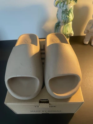 Yeezy slide - Säljer ett par stilrena YZY Slide tofflor från Adidas i beige färg. Bra skick! Skriv vid fler frågor!