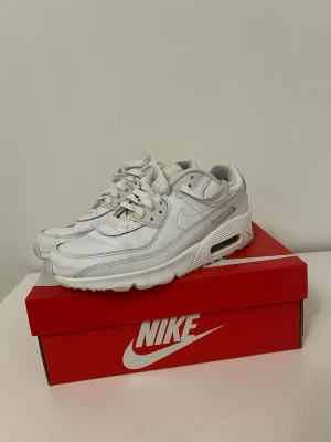 Nike Air Max 90 vita sneakers - Säljer ett par klassiska Nike Air Max 90 sneakers i helvitt. Skorna har en chunky sula med synlig Air-enhet, ovandel i läder och mesh samt ikoniska swoosh-loggan på sidan. Perfekta för dig som gillar stilrena och tidlösa sneakers.