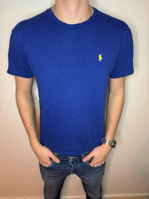 Blå t-shirt från Ralph Lauren - Snygg blå t-shirt från Ralph Lauren med klassisk gul logga broderad på bröstet. T-shirten har rund halsringning och korta ärmar. Perfekt basplagg med stilren design som passar till jeans eller shorts. Storlek M och suveränt skick! 9/10!!! Endast 199 kr men kan gå ner vid snabb och smidig affär 💙📦 // studio II Resell 