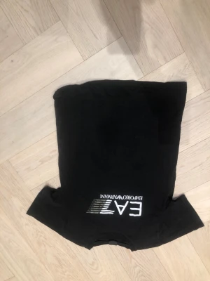 Svart EA7 t-shirt från Armani - Säljer en svart t-shirt från EA7 Emporio Armani med vit logga framtill. Klassisk passform och rund halsringning. Perfekt för dig som gillar stilrena märkesplagg och vill ha något enkelt men ändå snyggt i garderoben.