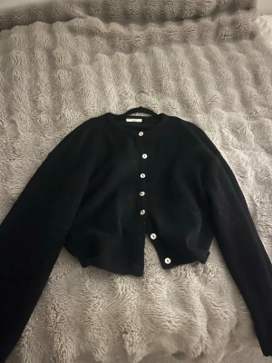 Svart kofta från ginatricot  - Mysig svart kofta från Gina med rund halsringning och vita knappar framtill. 