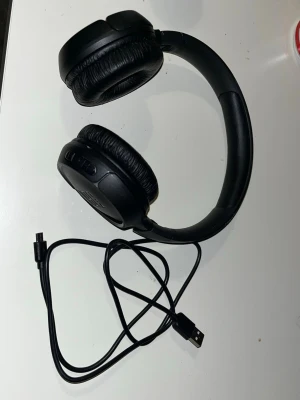 Svarta over-ear trådlösa hörlurar - Snygga svarta over-ear hörlurar med mjuka, vadderade kåpor och justerbart huvudband. Hörlurarna har inbyggda knappar på sidan och laddas via medföljande USB-kabel. Perfekta för musik, gaming eller videos. Tillverkade i plast och konstläder.