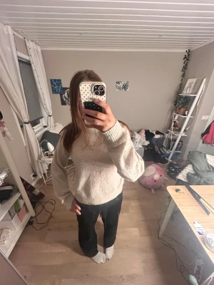 Beige stickad tröja med rund hals - Mysig beige stickad tröja med rund hals och långa ärmar. Tröjan har en avslappnad passform och ribbstickade muddar vid ärmslut och nederkant. Perfekt för lager-på-lager och enkel att matcha med olika outfits.