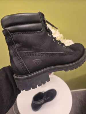 Tamaris svarta kängor med grov sula 37 - Säljer ett par svarta kängor med snörning och grov sula. Kängorna har vadderat skaft och är tillverkade i mocka och läder. Snygg detalj med diskret logotyp på sidan. Perfekta för dig som vill ha en stilren och robust look.