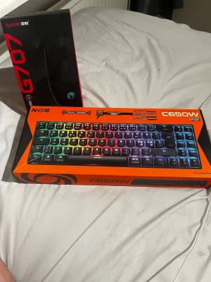 NOS C650W RGB tangentbord & RAIHU G707 mus - Säljer ett NOS C650W RGB tangentbord med snygg regnbågsbelysning och kompakt design, samt en RAIHU G707 gamingmus. Tangentbordet har svart plastchassi och färgglada LED-tangenter. Perfekt för gaming eller datoranvändning hemma.