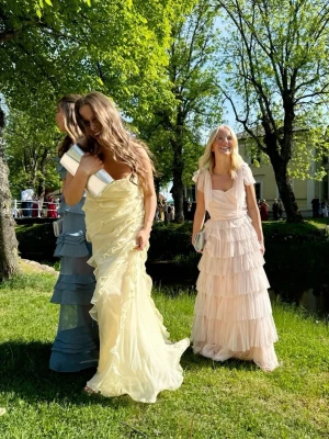 Ljusgul lång bal/fest klänning med volanger - Säljer en drömmig ljusgul lång bal/fest klänning med volangdetaljer och omlottkänsla. Klänningen är ärmlös, perfekt för student eller bal. Materialet är lätt och ger ett elegant fall. Lånade bilder