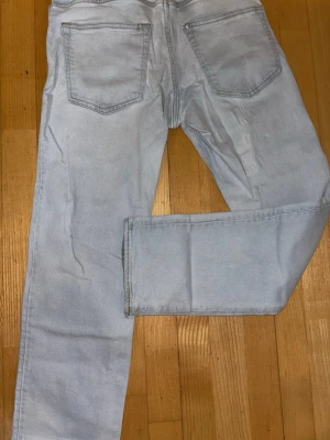 Ljusblå raka jeans - Säljer ett par ljusblå jeans med rak passform och klassiska fem fickor. Jeansen har bälteshällor och stängs med knapp och dragkedja. Perfekta för en avslappnad och trendig look.
