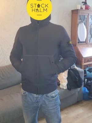 Stone island herr jacka  - Snygg marinblå  Stone Island skaljacka med klassisk patch på vänster ärm. Jackan har hög krage, dragkedja framtill och två snedställda fickor. Materialet ser ut att vara slitstarkt och jackan är otroligt bra skick som nytt