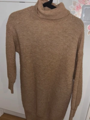 Beige polotröja stickad - Mysig beige stickad polotröja i längre modell. Tröjan har ribbstickad struktur, lång ärm och hög polokrage. Perfekt för lager på lager och en avslappnad stil. Materialet känns mjukt och värmande.