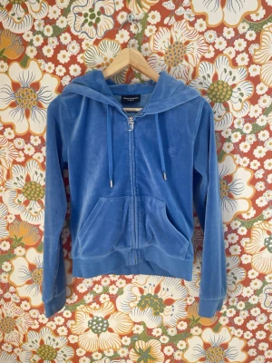 Blå velour hoodie från Juicy Couture - Säljer en blå zip-up hoodie från Juicy Couture i mjuk velour. Hoodien har huva med dragsko, två fickor fram och ribbade muddar vid ärmslut och nederkant. Perfekt för en chill och trendig look.