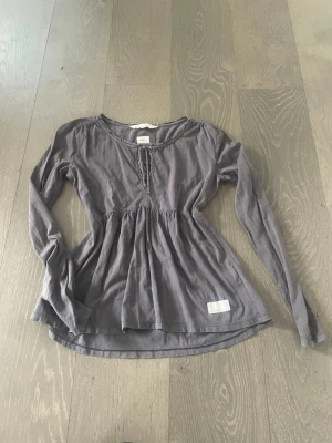 Babydoll❤️ - Snygg grå blus från Odd Molly med lång ärm och avslappnad passform. Blusen har rundad halsringning med dekorativt knytband och lätt rynkad midja för en feminin siluett. Tillverkad i mjukt bomullstyg och har en liten logolapp nedtill.