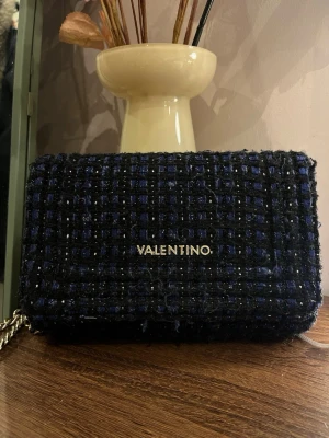 väska Valentino - Säljer en snygg kuvertväska från Valentino i mörkblått och svart rutigt tyg. Går att använda som både väska och clutch! Varan har lite slitningar och en defekt på undersidan,! Priset kan diskuteras