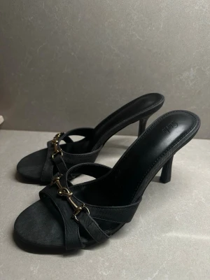 Grå/svarta klackskor  - Säljer ett par svarta klackar med gulddetalj framtill. Stilrena och passar perfekt till fest, middag eller utekväll.  • Klackhöjd: 8,8 cm • Skick: aldrig använda  • Nypris: 228 kr • Märke: Shein  Säljes då de inte kommer till användning.