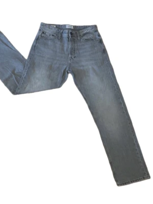 Grå jeans från Jack & Jones - Snygga grå jeans från Jack & Jones med klassisk femficksmodell och raka ben. Jeansen har knappgylf och är tillverkade i mjukt denimtyg som ger en avslappnad look. Perfekta för dig som gillar en enkel och stilren stil.