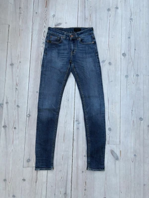 Blå skinny jeans ifrån Tiger of Sweden - Säljer ett par blå skinny jeans ifrån Tiger of Sweden med klassisk femficksdesign. Jeansen har en snygg tvätt och smala ben som sitter tight hela vägen ner. Perfekta till sneakers eller boots och passar till det mesta i garderoben.