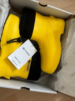 Gula stövlar från Fubuki - Säljer ett par riktigt coola gula stövlar från Fubuki, modell Niseko 2.0 Low. De har svart skaft med dragsko och slitstark svart sula med grovt mönster för bra grepp. Perfekta för regniga dagar och outdoor-äventyr samt varm fodring för att klara av vinterkyla.