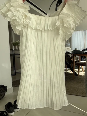 Vit plisserad klänning från Zara - Supersöt vit kortklänning från Zara med plisserad design och stora volangärmar. Offshoulder-modell som ger en trendig look. Perfekt för sommarens alla tillfällen. Tillverkad i ett lätt och luftigt material.