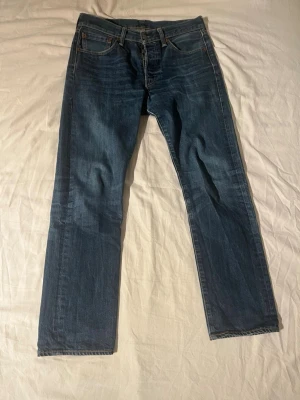 Levi's 501 blå jeans W31 L30 - Hej! Klassiska Levi's 501 jeans i mörkblå tvätt med raka ben. Jeansen har den ikoniska läderpatchen bak i midjan och knappgylf. Snygg slitning och kontrastsömmar ger en tidlös look. Perfekta till sneakers eller boots. Tveka inte på att höra av dig om du har frågor!
