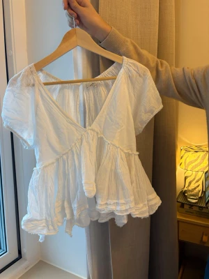 Vit blus med puffärm och volang - Säljer en vit blus från Urban Outfitters. Perfekt till våren🌼  Modell med V-ringning framtill, knytning i ryggen och fint fall i tyget, (volang)  Storlek: passar S–M beroende på hur man vill att den sitter Färg: Vit Skick: Fint skick Obs: Behöver strykas!!  Djur- och rökfritt hem. Snabb frakt och packar väl🙌